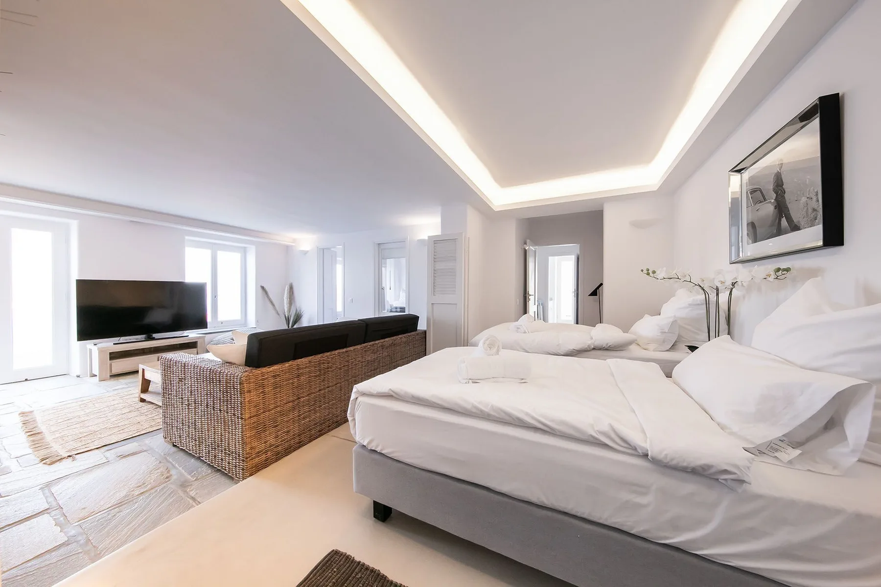 A bright bedroom with a large bed and a seating area beside the television.