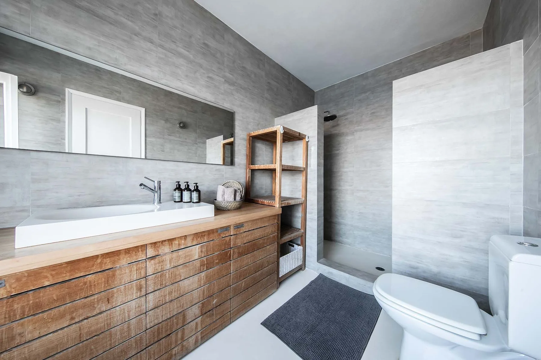 A modern bathroom with a long wooden vanity and a walk-in shower.