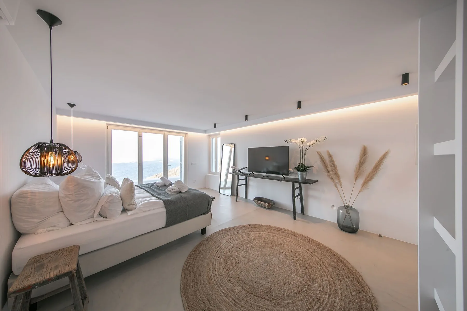 A bright bedroom with a bed, a television, and large windows.