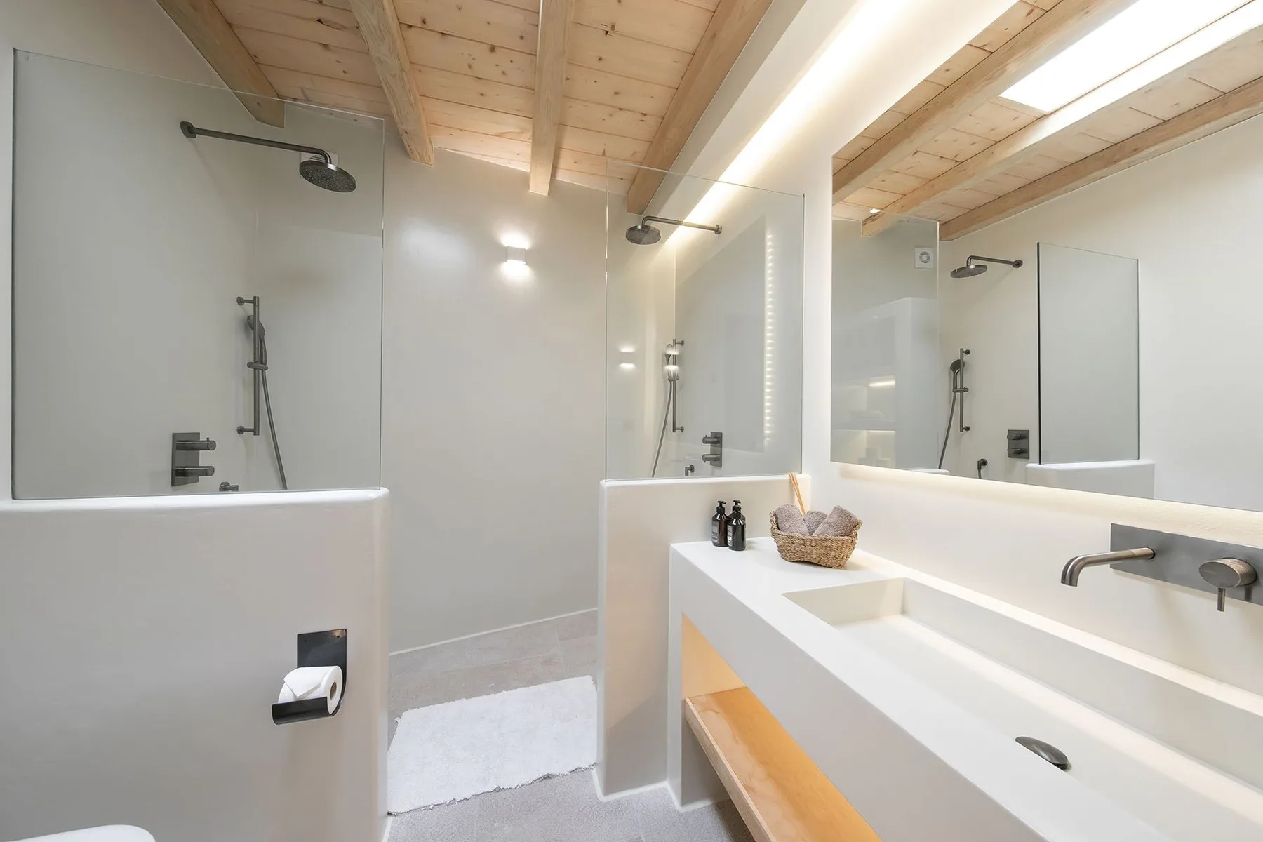 A bright bathroom with a walk-in shower, a long sink counter, and a wood-paneled ceiling.
