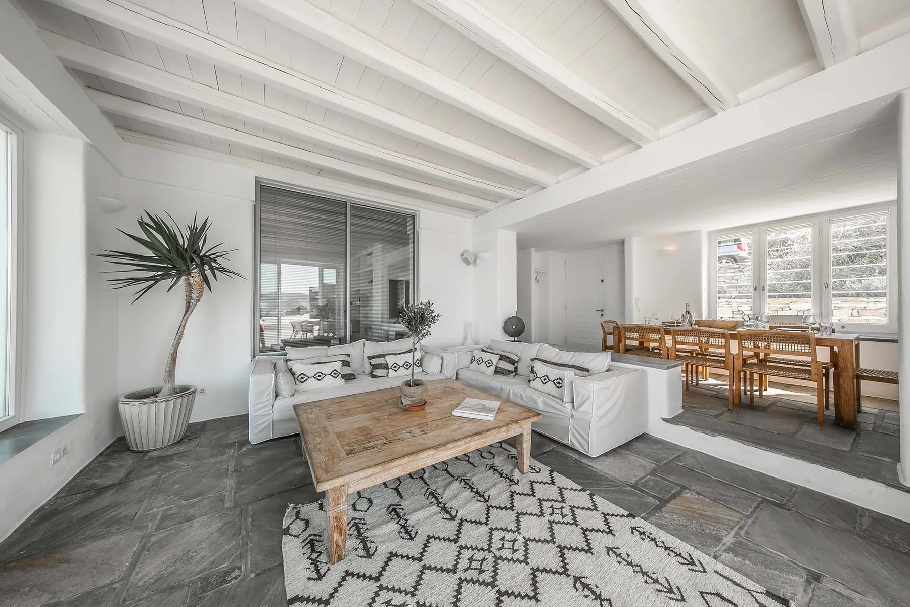 A bright living room with seating, a coffee table, and a dining area by the windows.