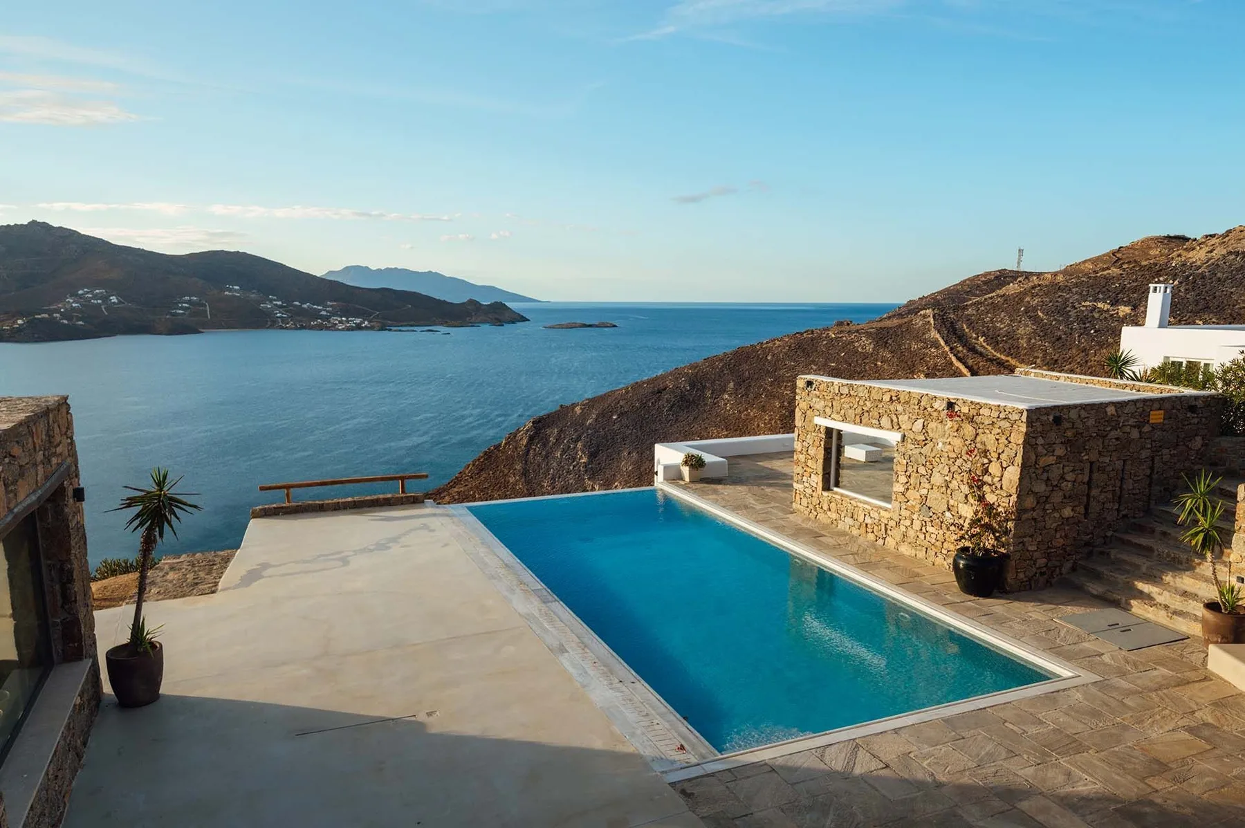 A swimming pool and stone terrace overlook the sea and surrounding hills.