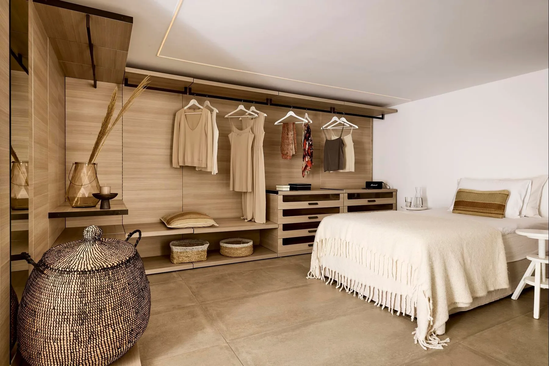 Un dormitorio con una cama junto a un perchero abierto y almacenamiento bajo.