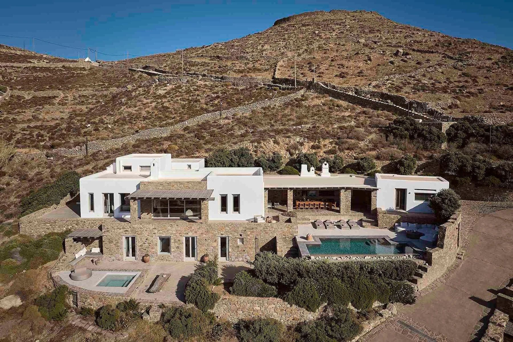 Una villa moderna se encuentra en una ladera seca, con una piscina al frente.