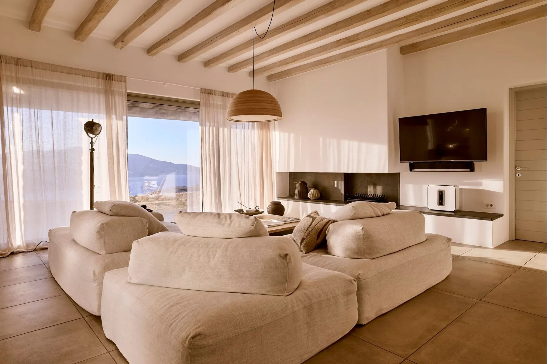 Una sala luminosa con asientos amplios, un televisor en la pared y grandes ventanas con cortinas.