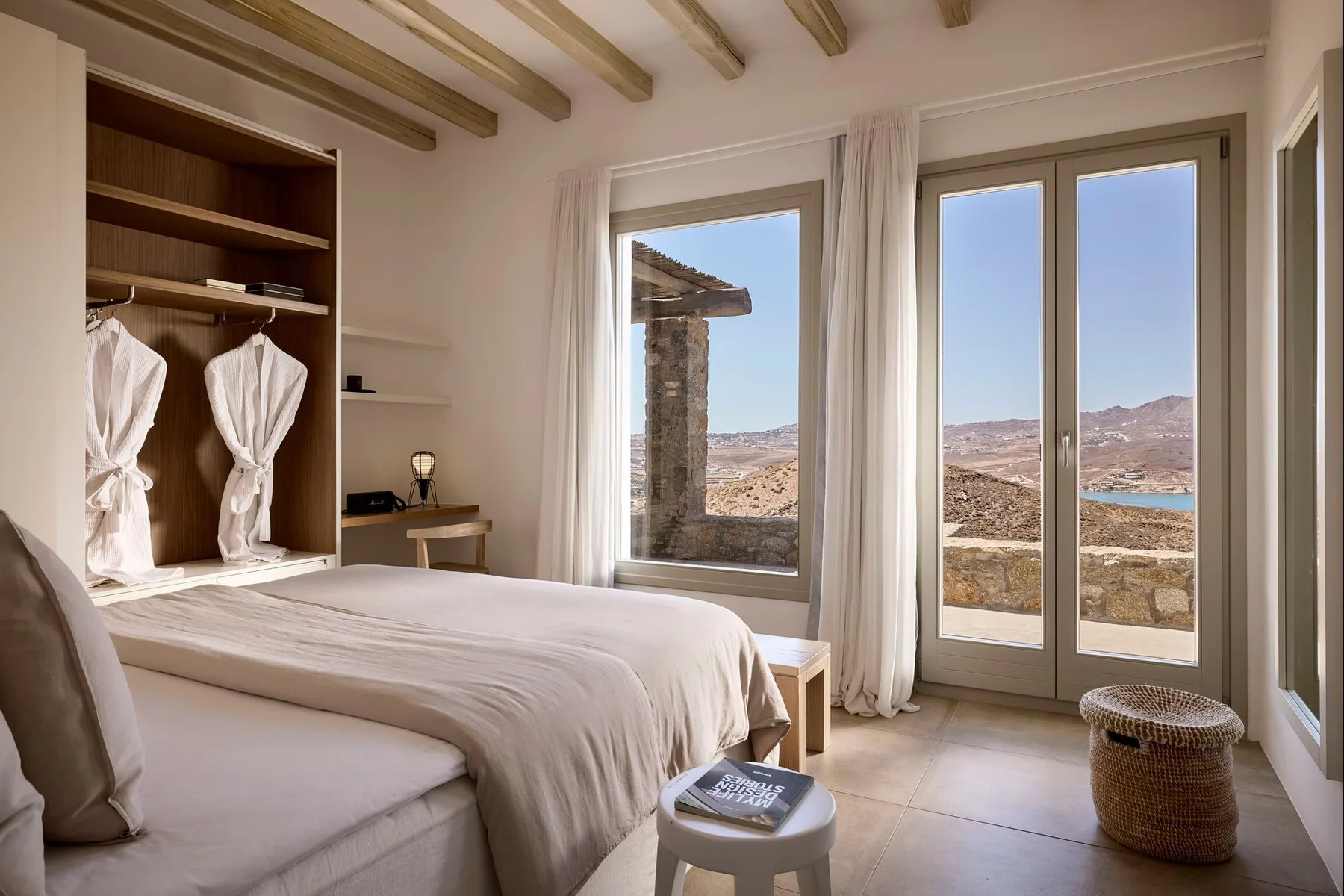 Un dormitorio luminoso con una cama junto a ventanales que dan a un paisaje seco.