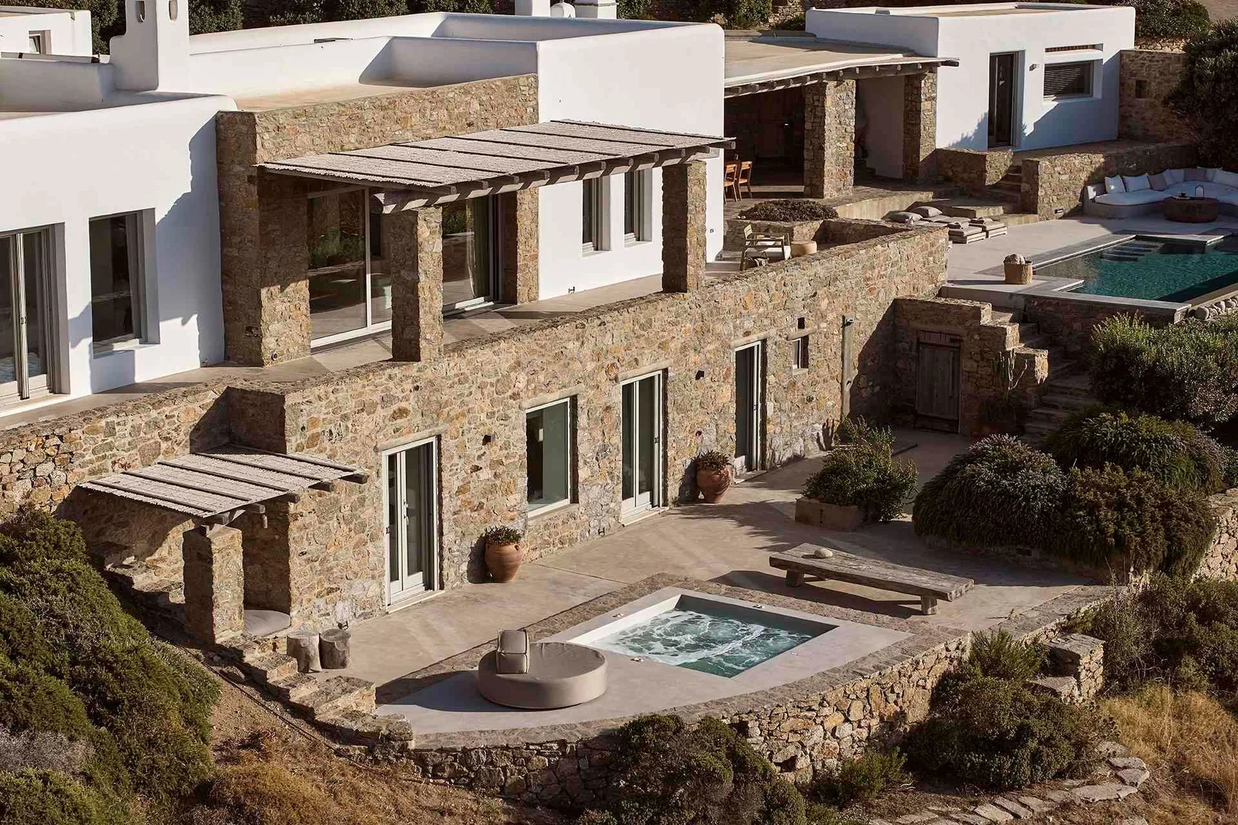 Exterior de una villa revestida de piedra con una piscina pequeña y un patio sombreado.