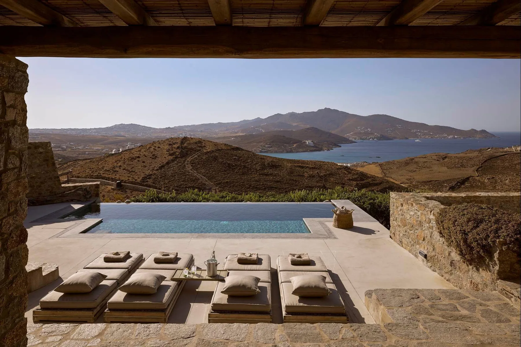 Una terraza con piscina y asientos de descanso ofrece vistas a una bahía y colinas.