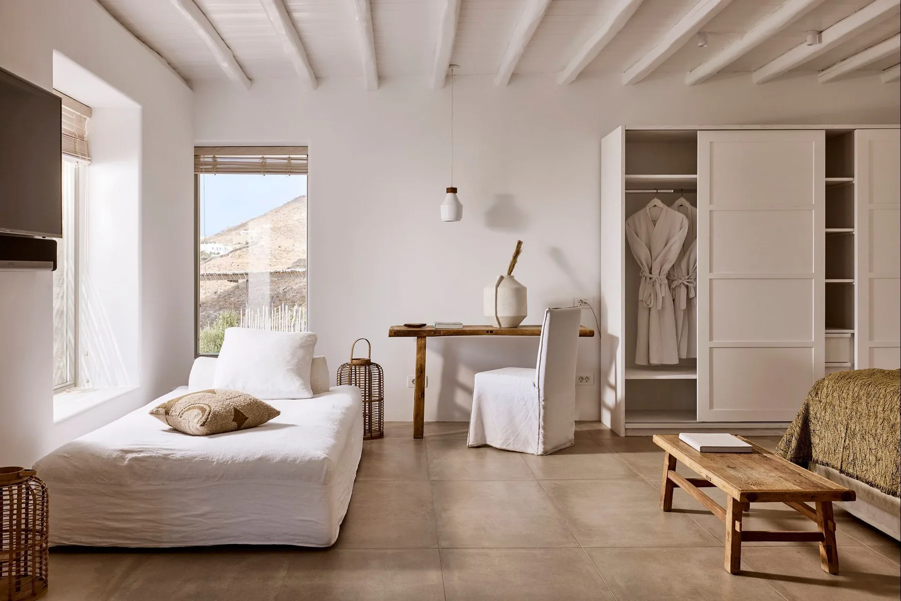 Un dormitorio luminoso con una cama, una mesa pequeña y un armario abierto.