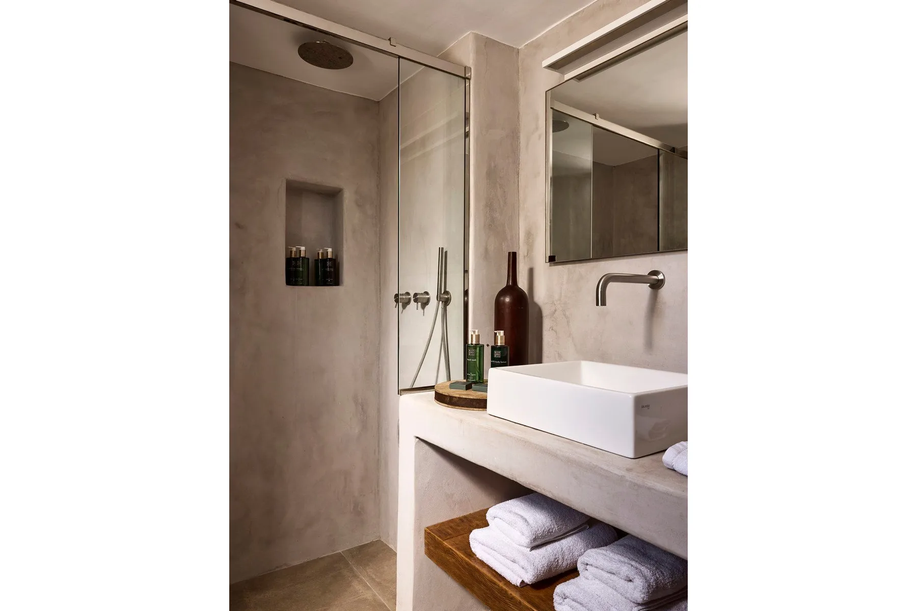 Un baño moderno con ducha de vidrio, lavabo sobre encimera y toallas dobladas.