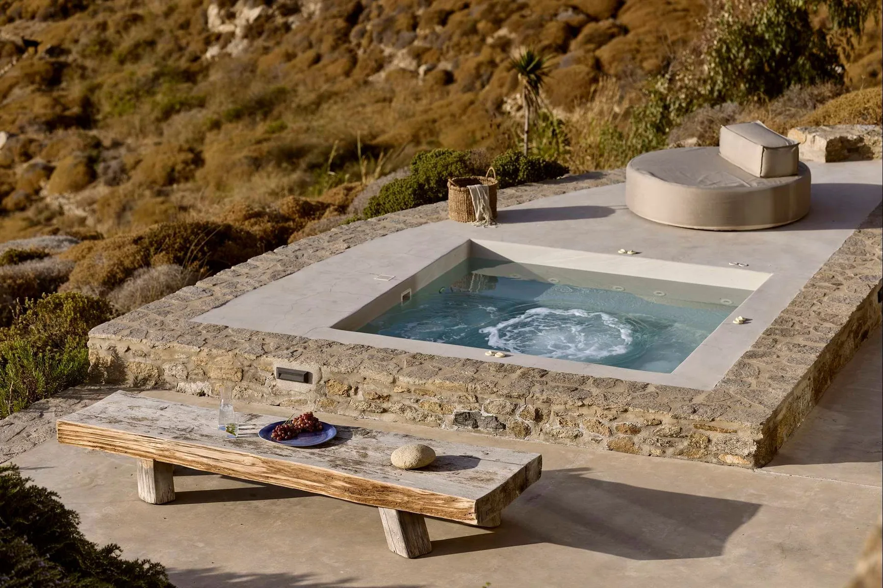 Una piscina al aire libre está junto a una zona circular elevada para sentarse, en un paisaje rocoso.