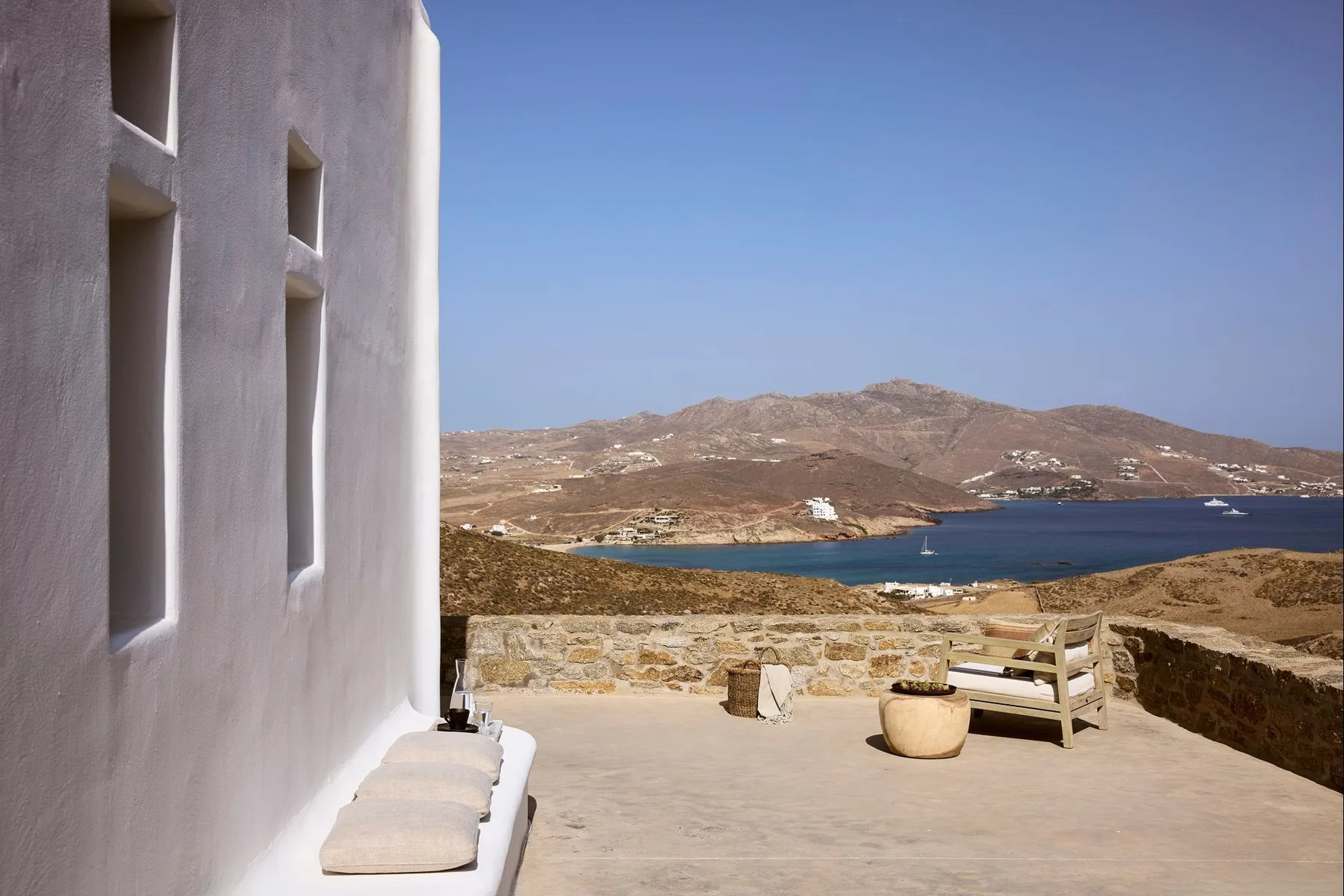 Una terraza soleada da a una bahía azul y un paisaje de colinas secas.