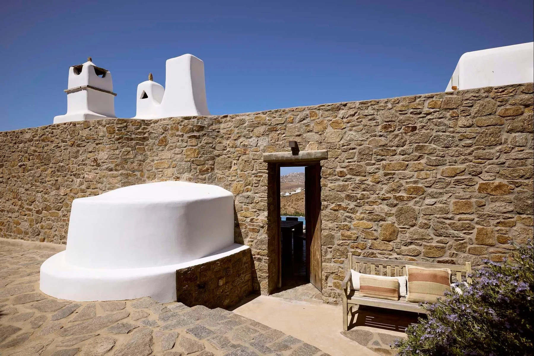 Un patio de piedra con una puerta estrecha y un banco blanco integrado.