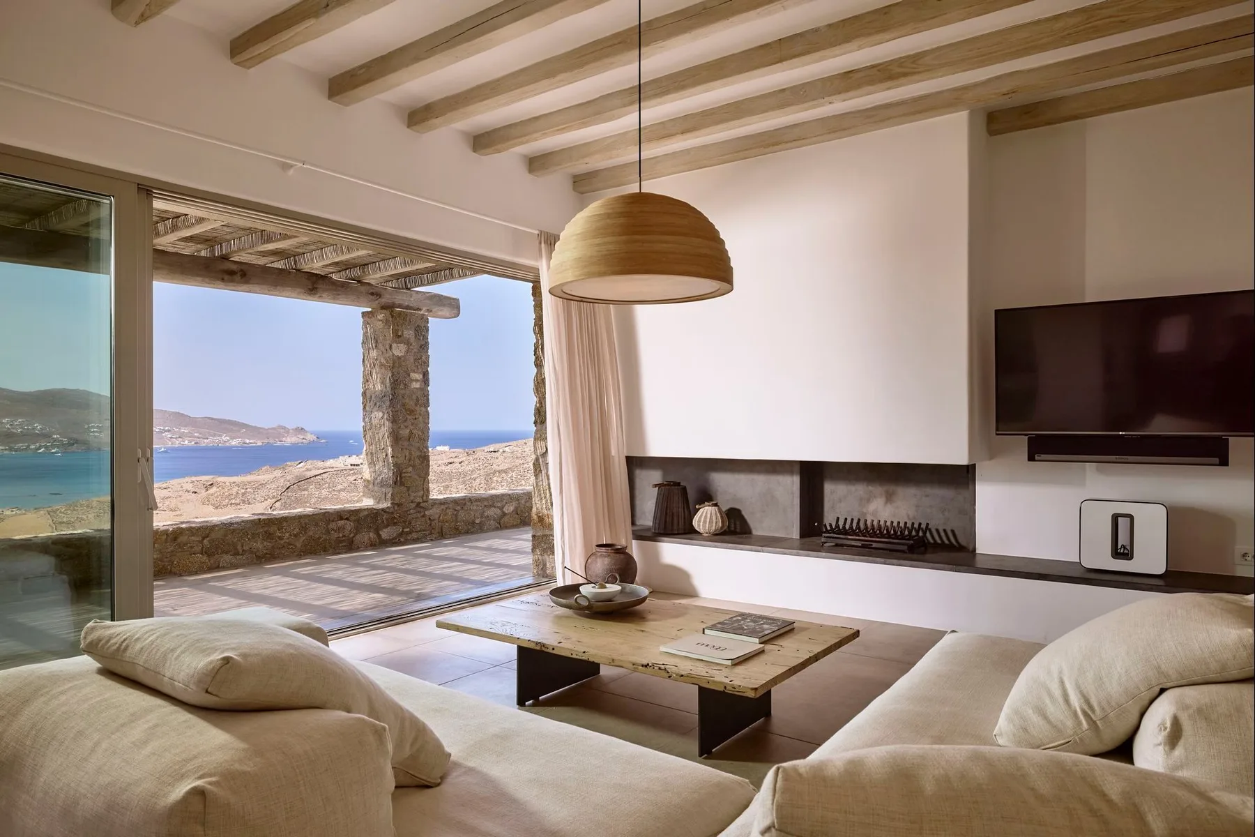 Una sala de estar se abre a una terraza junto al mar, con una mesa baja y una chimenea empotrada.