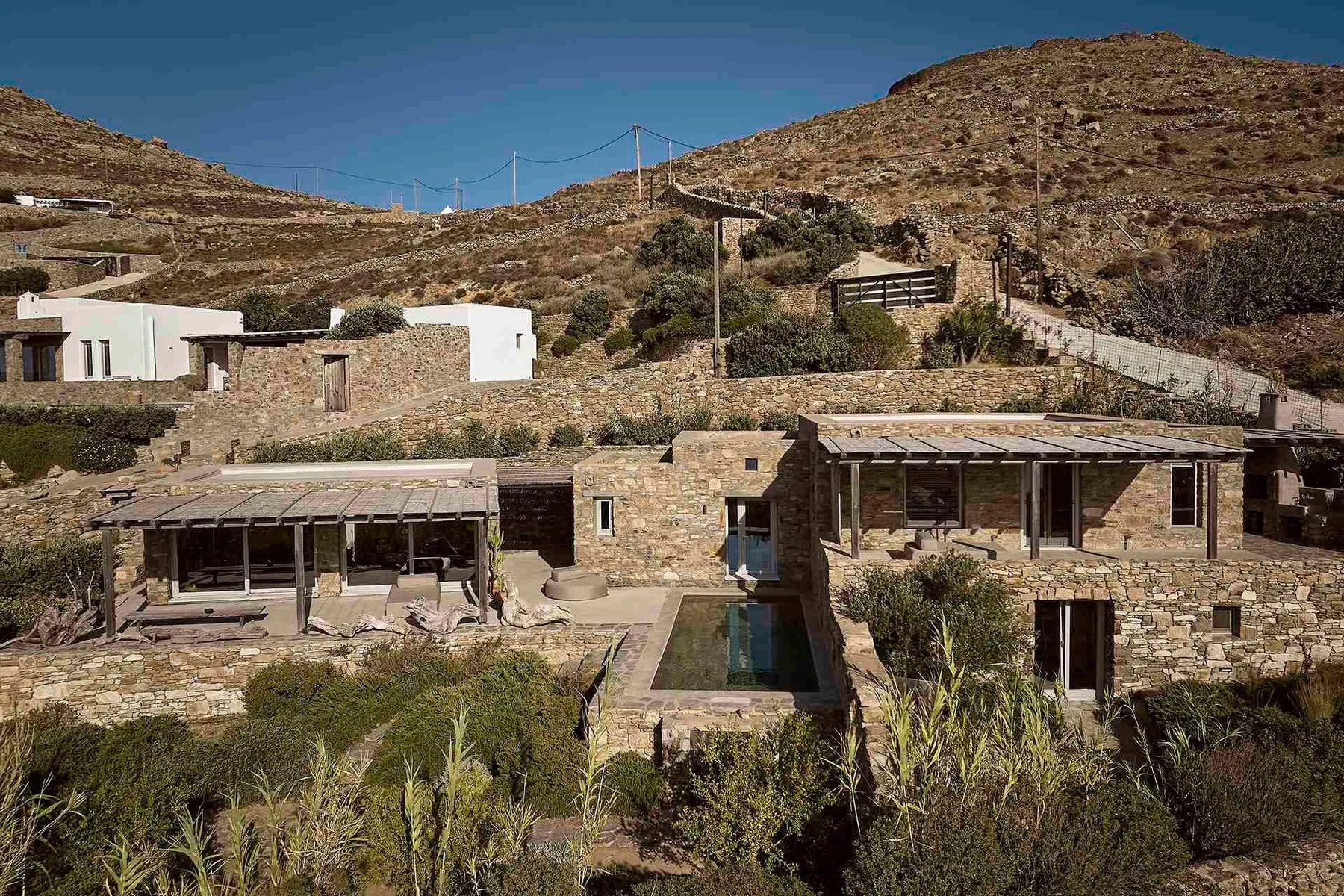 Edificios de piedra y una pequeña piscina se encuentran entre colinas secas y vegetación dispersa.