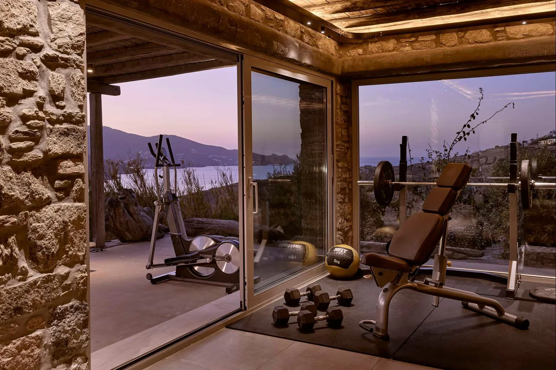 Un gimnasio con equipo de ejercicio y grandes ventanas con vista al agua.