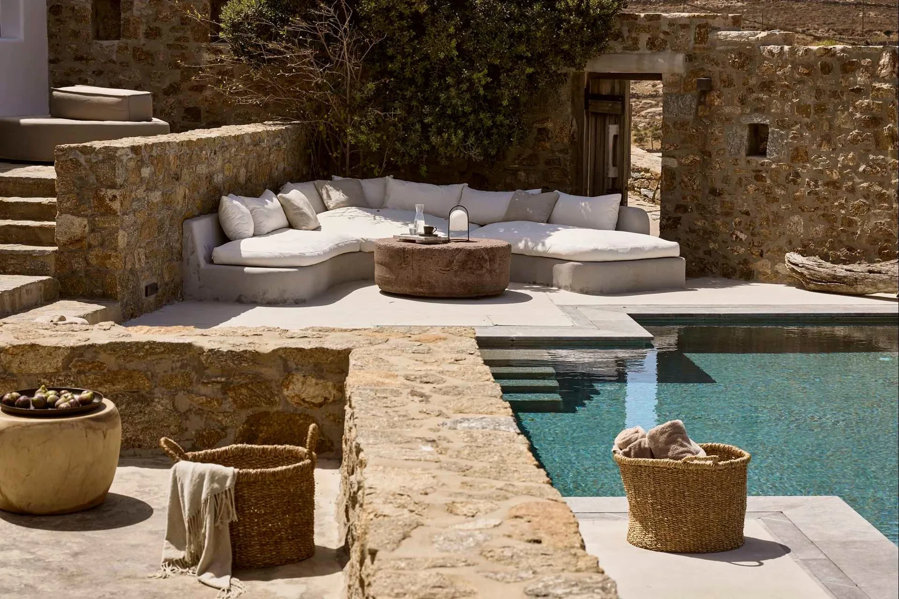 Una piscina al aire libre junto a un patio de piedra con asientos acolchados.