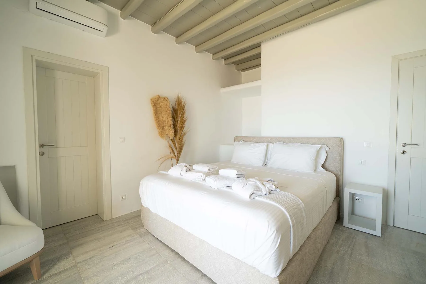 A bright bedroom with a neatly made bed and exposed ceiling beams.