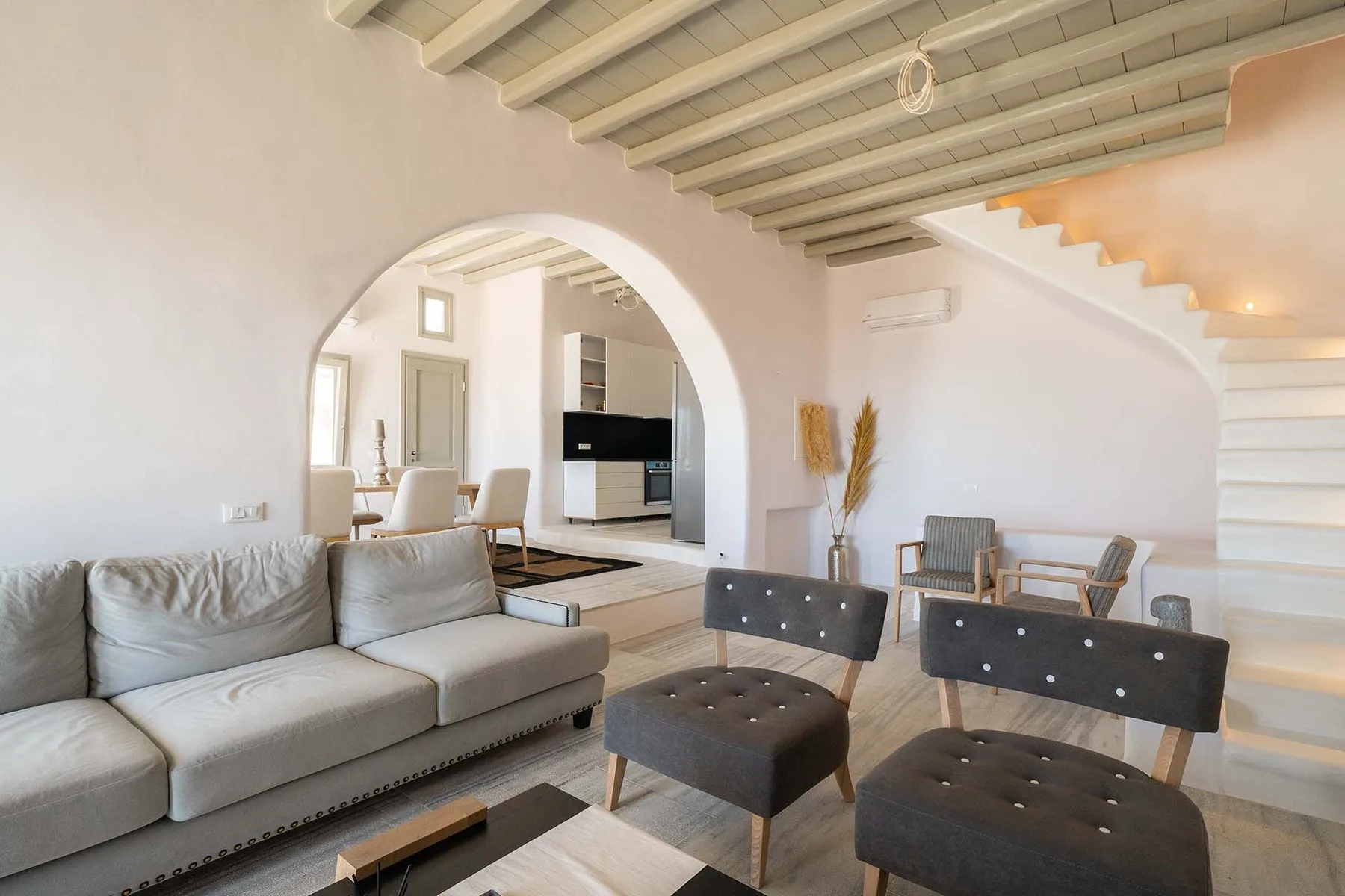 A living room with seating beneath a staircase and exposed ceiling beams.