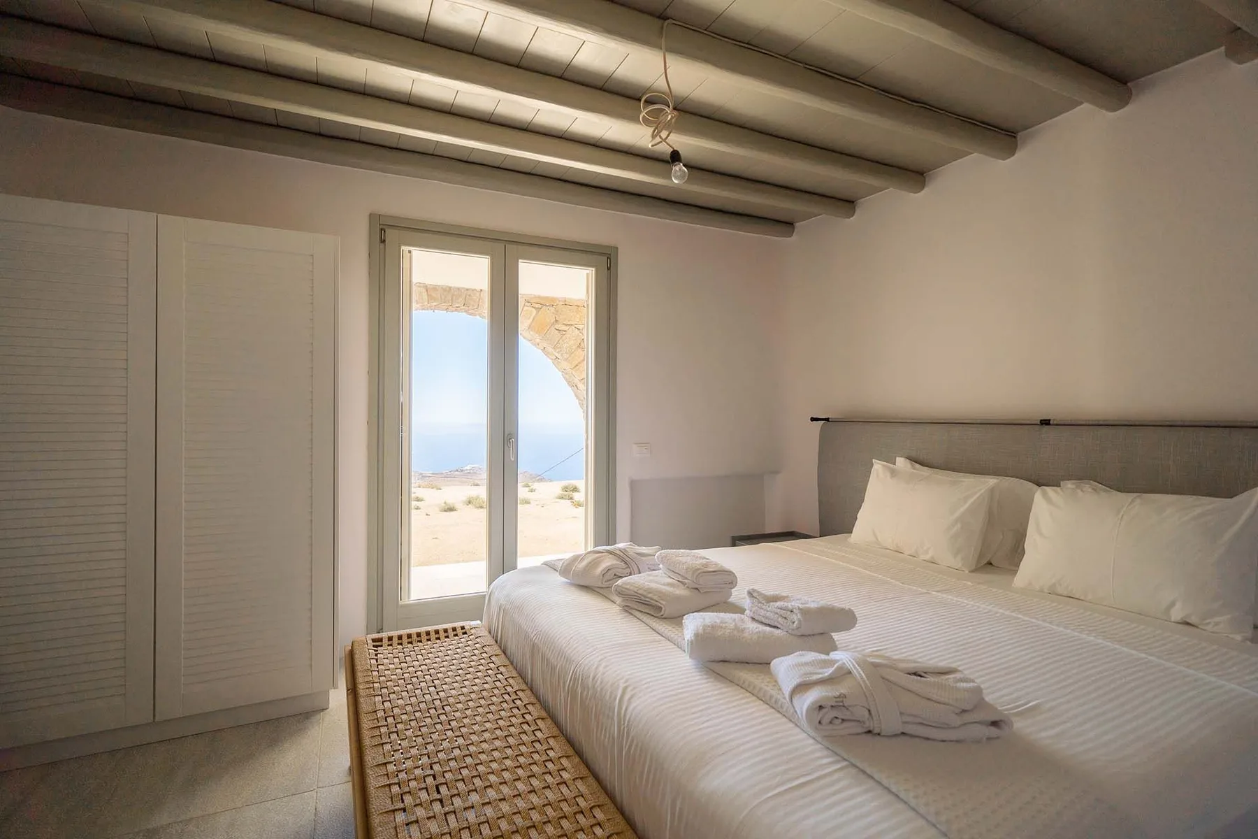A bright bedroom with a bed beside tall glass doors overlooking the sea.