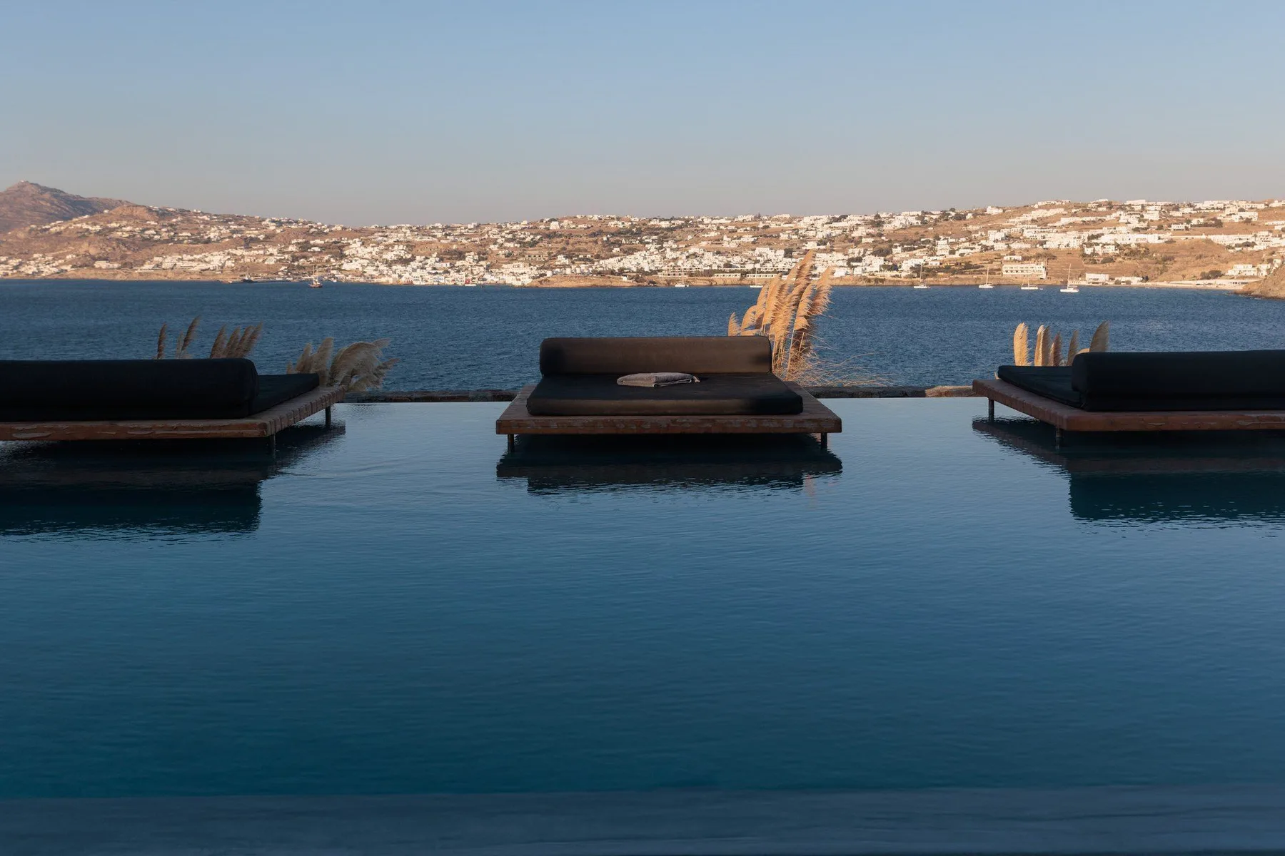 An infinity pool overlooks a blue bay and a hillside town.