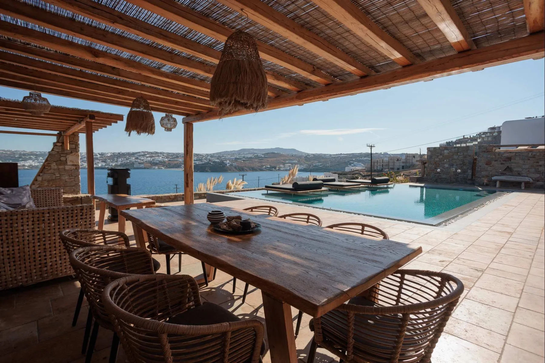 A shaded outdoor dining area overlooks a swimming pool and the sea.