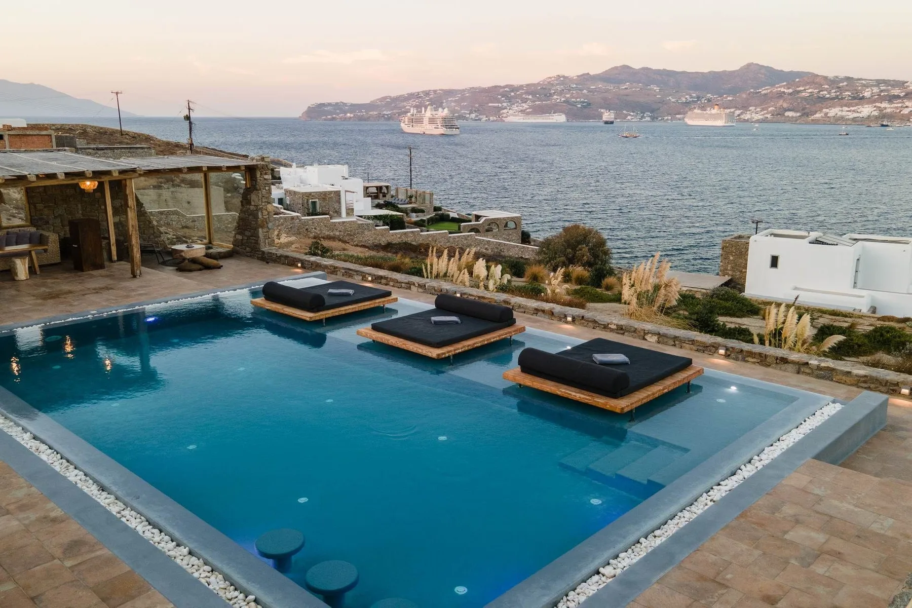 A swimming pool overlooks the sea, with floating lounge platforms on the water.