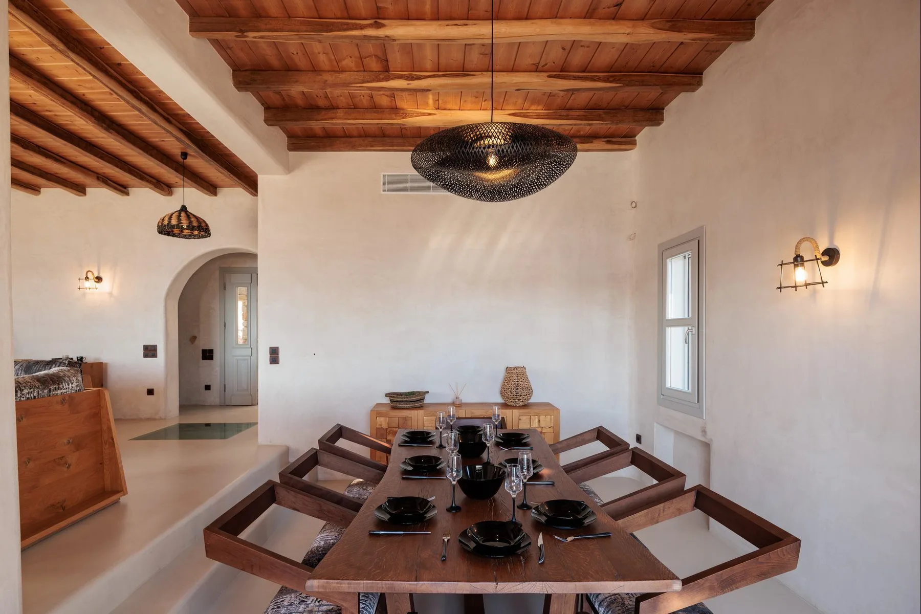 A dining room with a long wooden table beneath exposed ceiling beams.