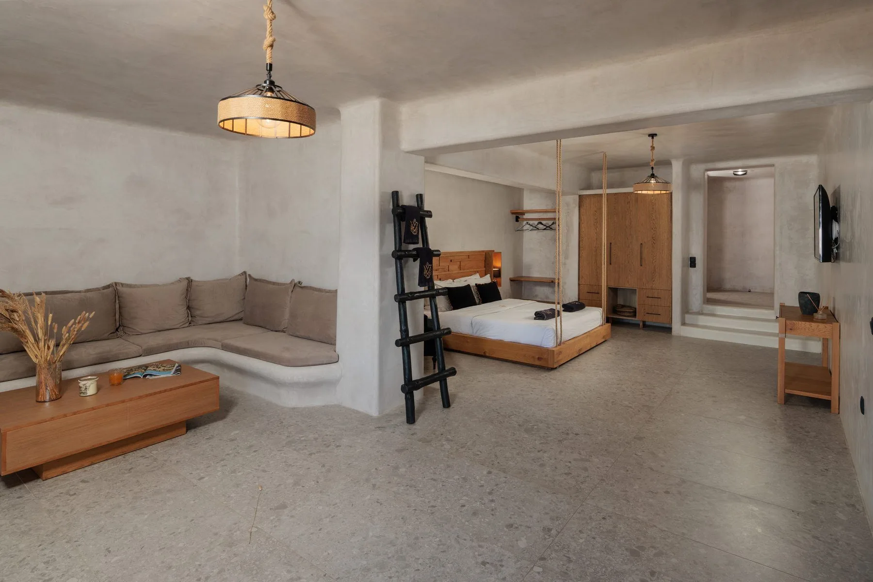 A bedroom and sitting area share an open space, with a bed and corner seating.