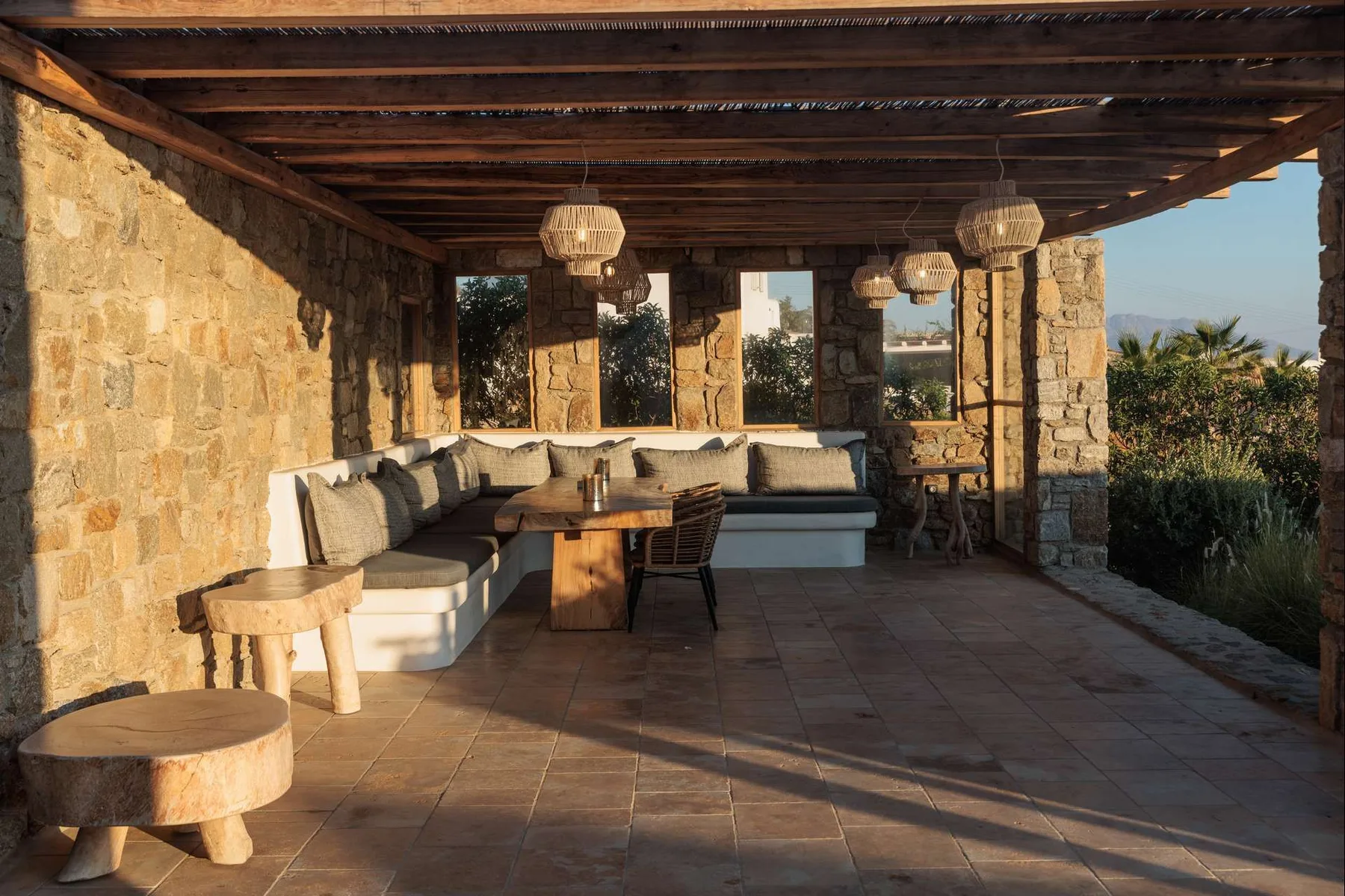 A covered stone patio features built-in seating around a wooden table.