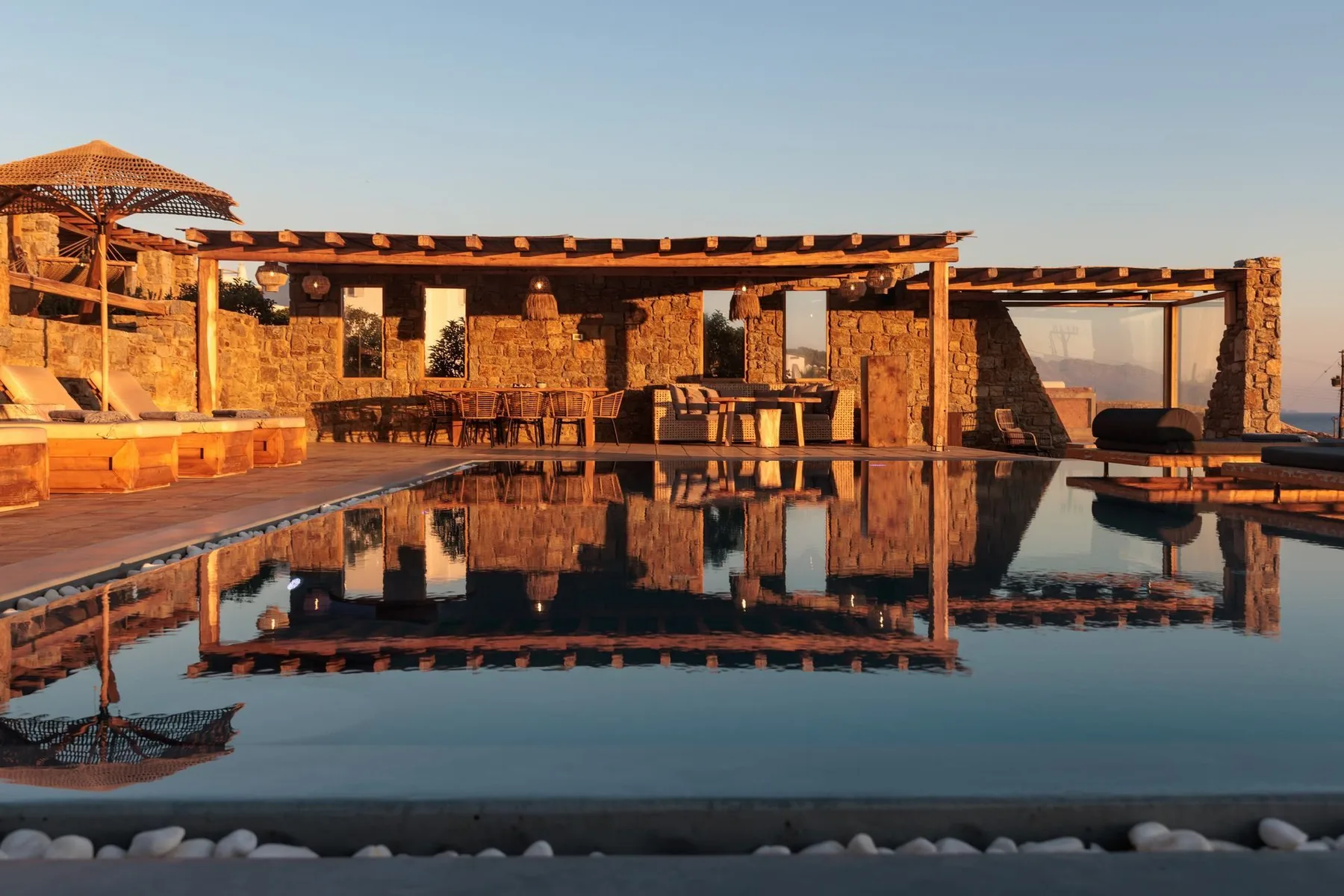 An outdoor pool reflects a stone building with open-air dining tables.