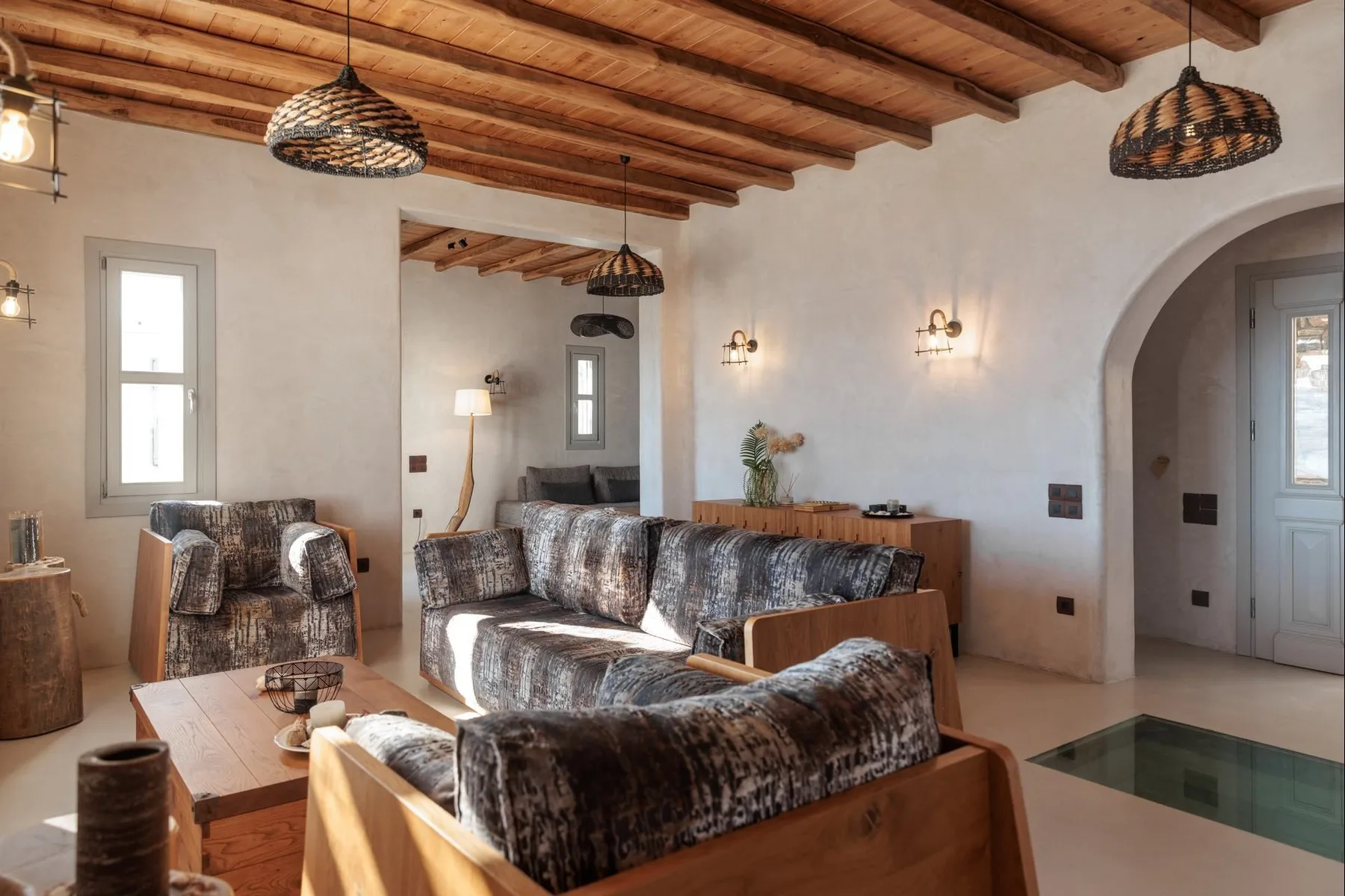 A living room with upholstered seating, wooden tables, and exposed ceiling beams.