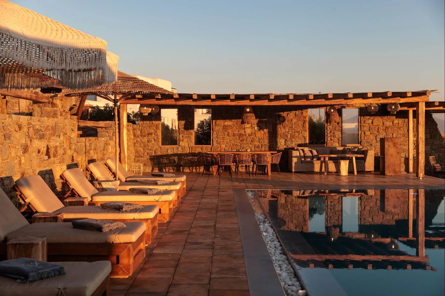 An outdoor poolside patio with lounge seating and a dining area in warm evening light.