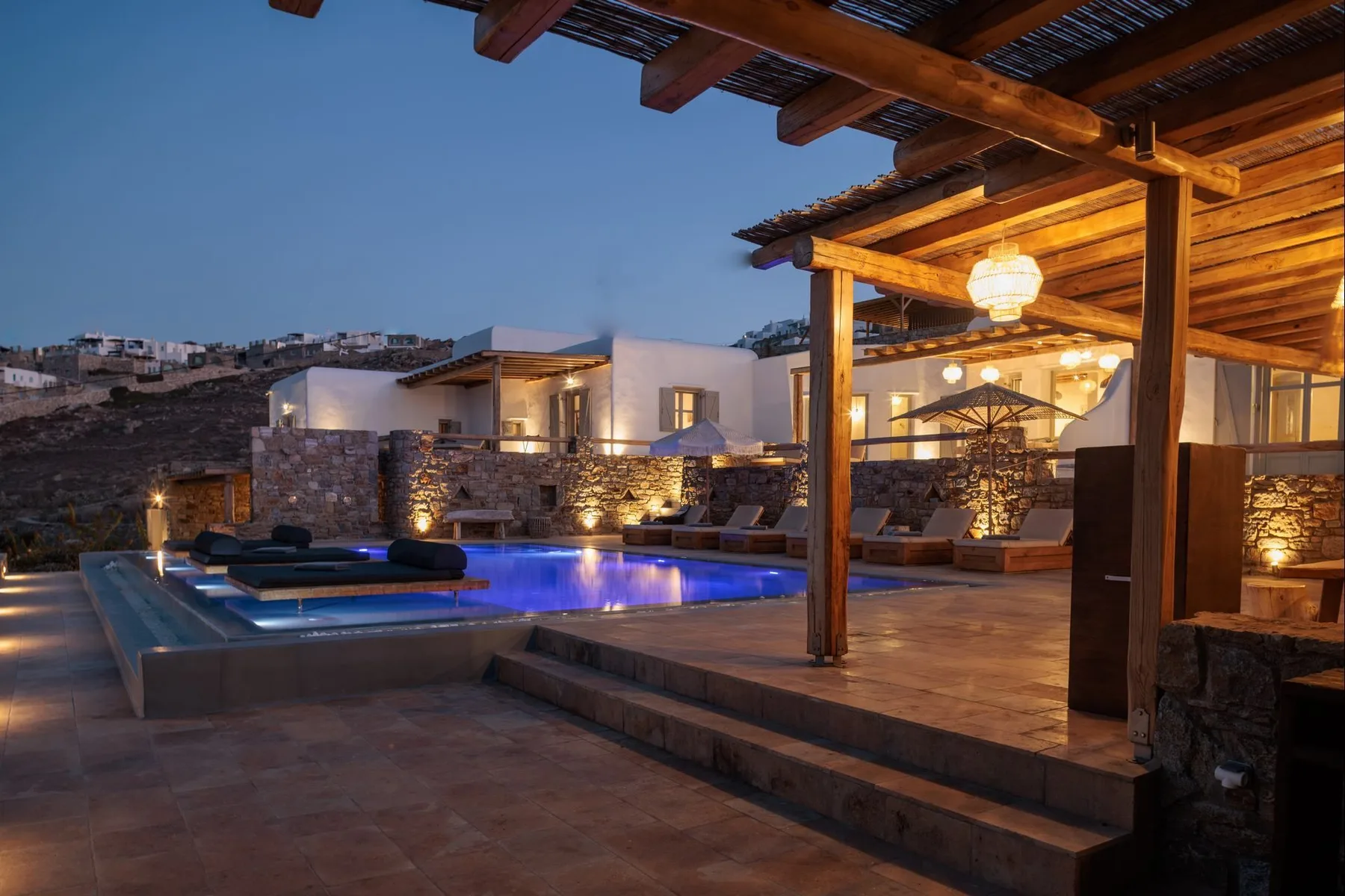 An outdoor pool beside a warmly lit wooden patio at dusk.