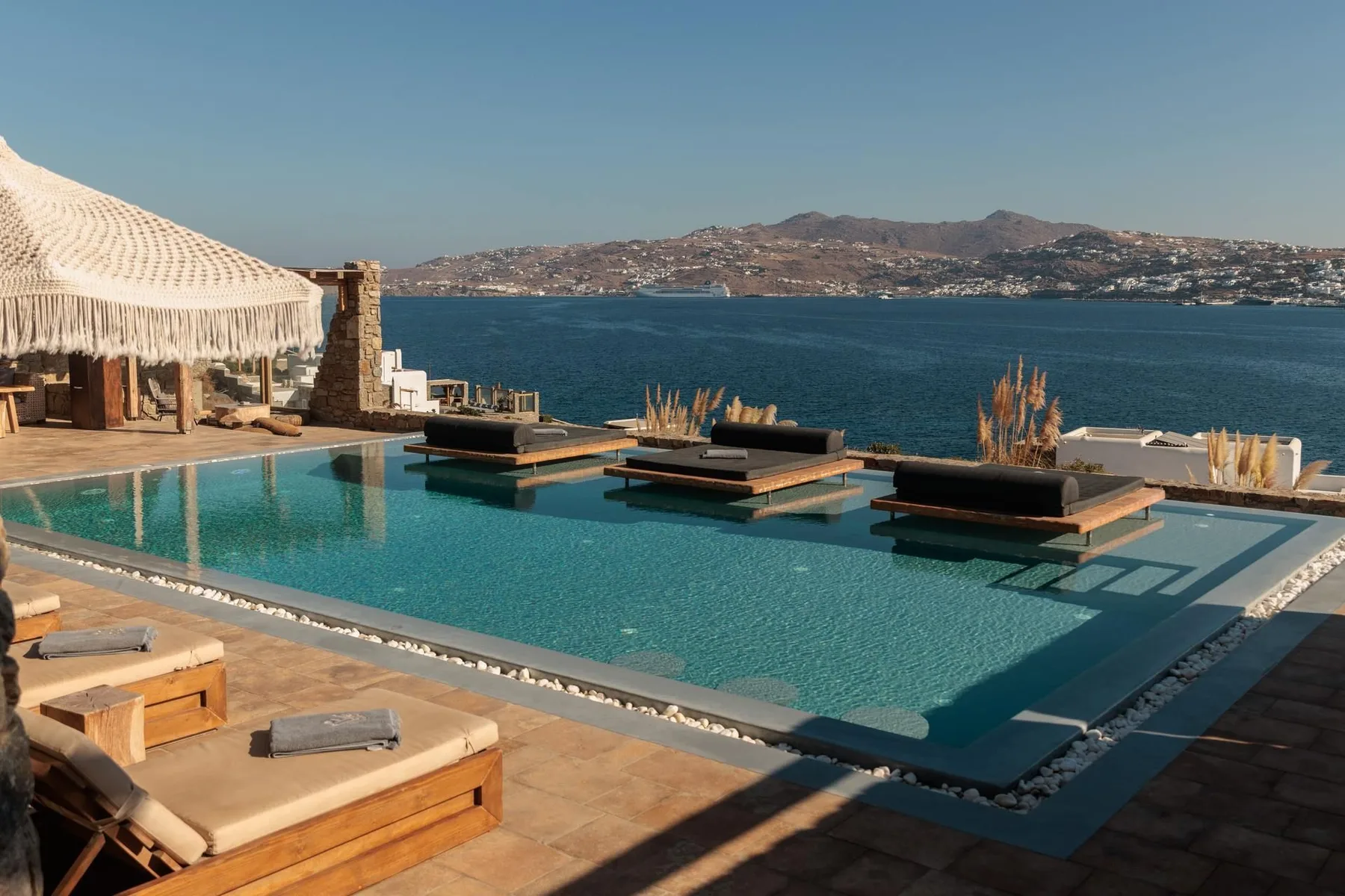 An outdoor infinity pool overlooks the sea, with cushioned loungers nearby.