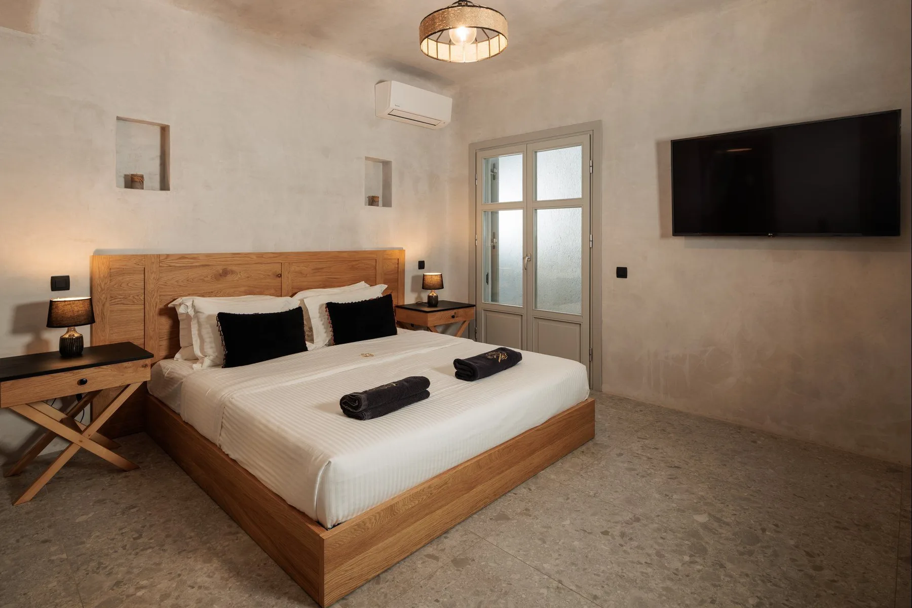 A bedroom with a large bed, bedside tables, and a wall-mounted television.
