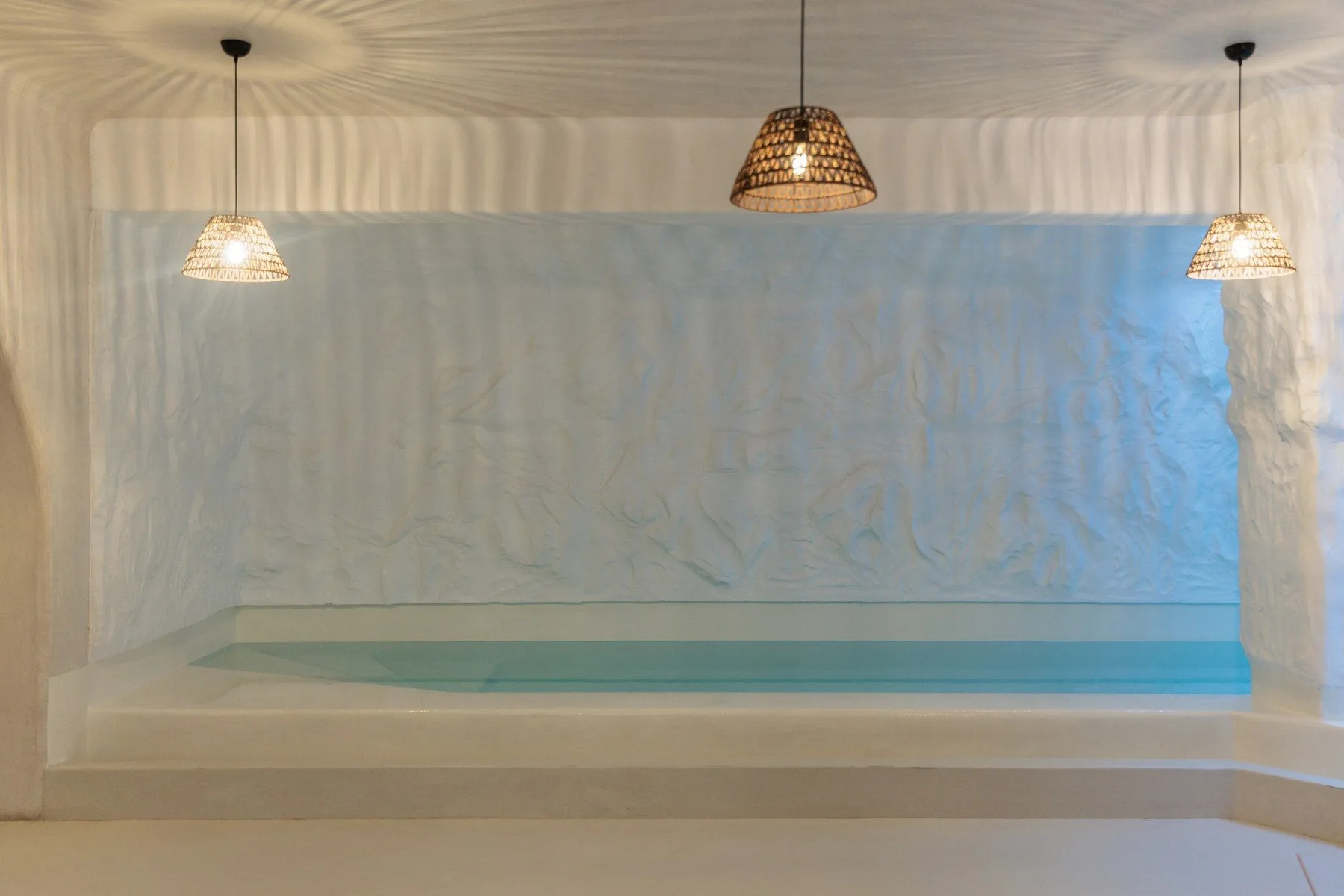 A recessed indoor pool sits beneath three hanging lights.