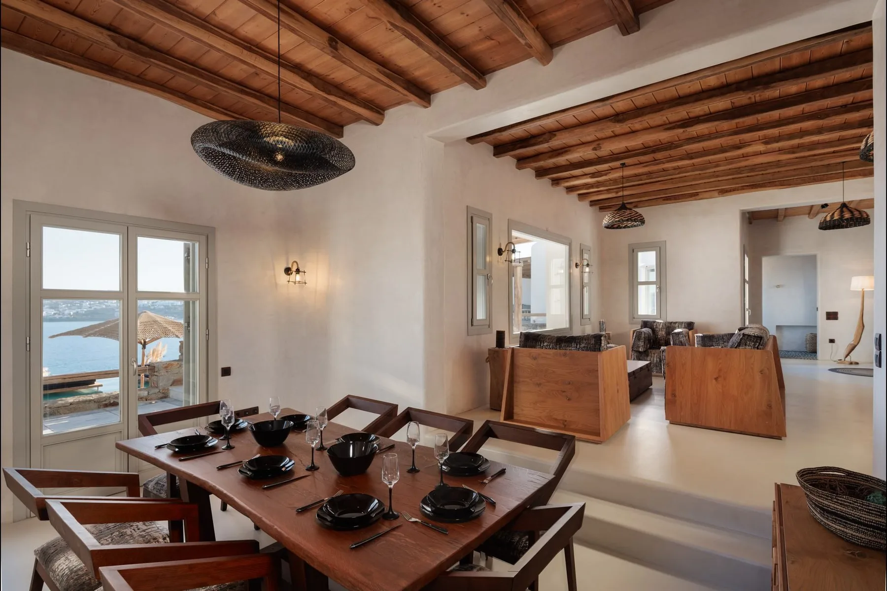 A dining area with a set table beside a living area under exposed wooden ceiling beams.