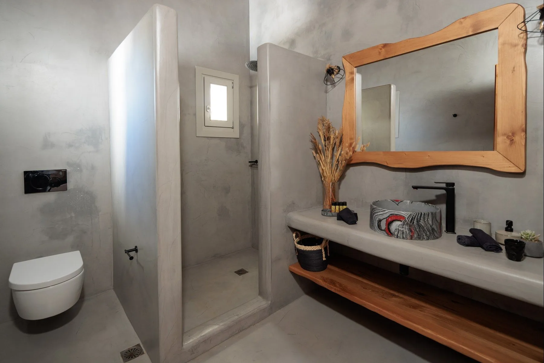 A bathroom with a glass shower, wall-mounted toilet, and a long vanity.