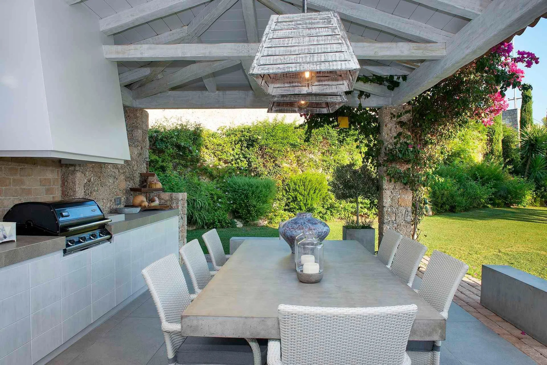 Comedor exterior cubierto con una mesa larga junto a un jardín.