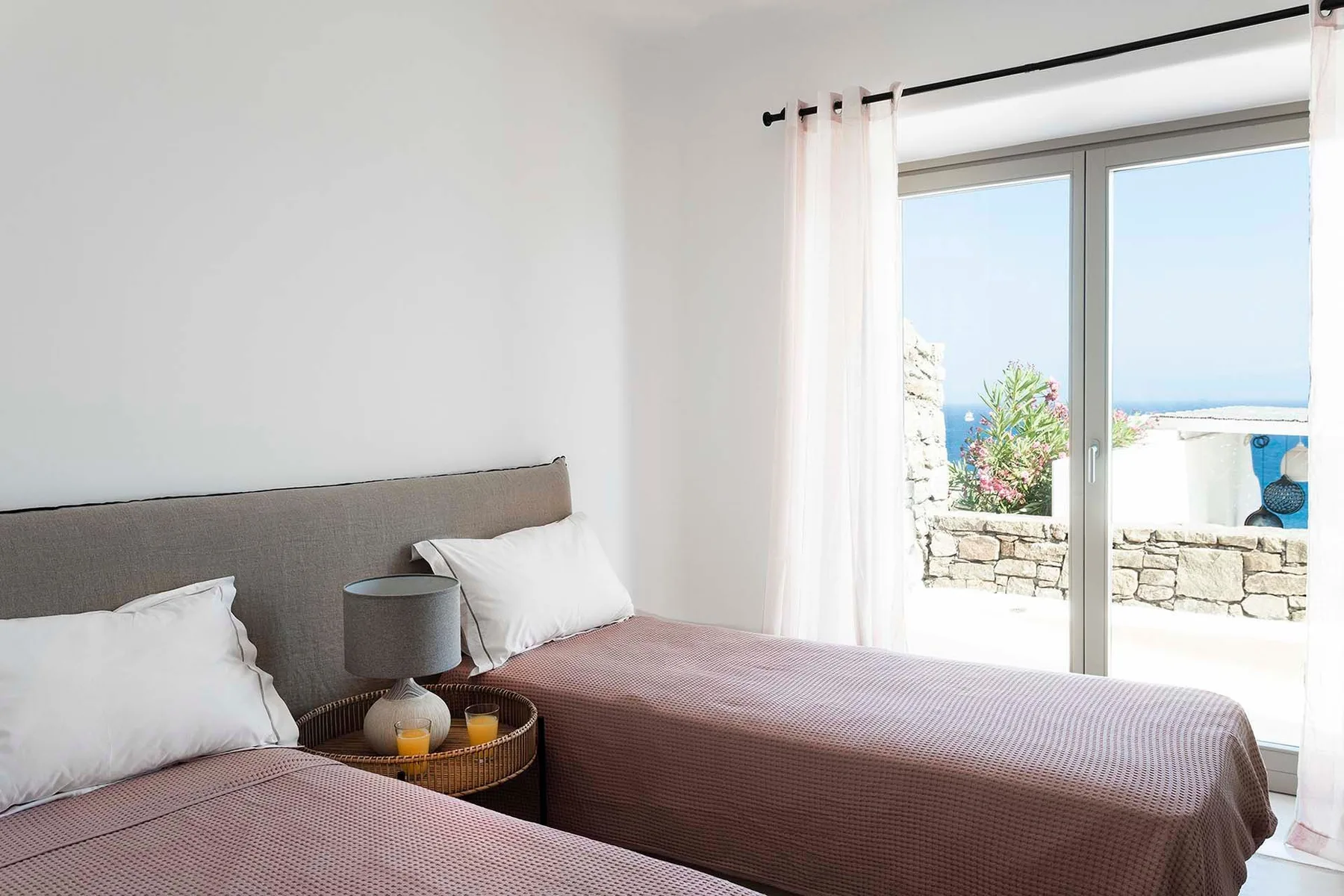 A bright bedroom with twin beds beside a large sliding glass door.