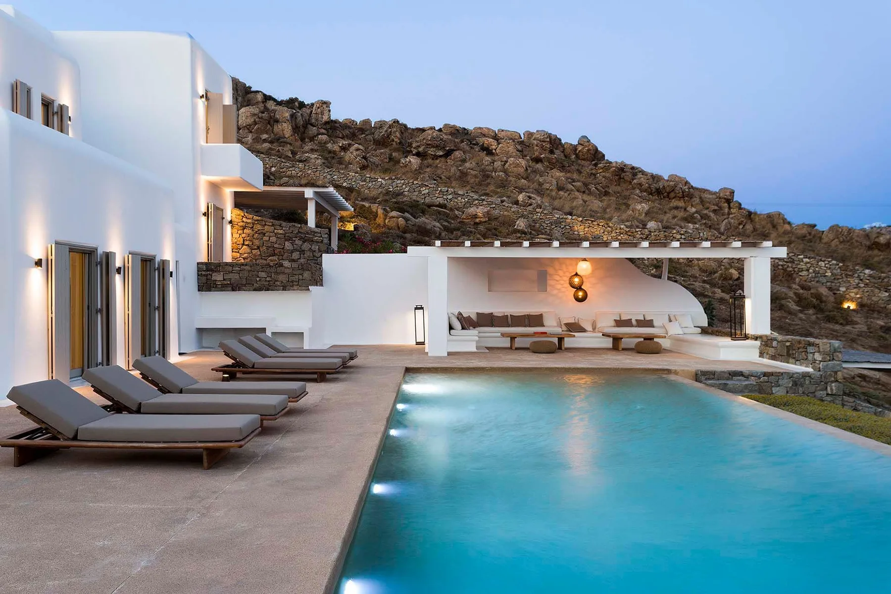 A modern white villa opens onto a turquoise pool, with loungers along the terrace.