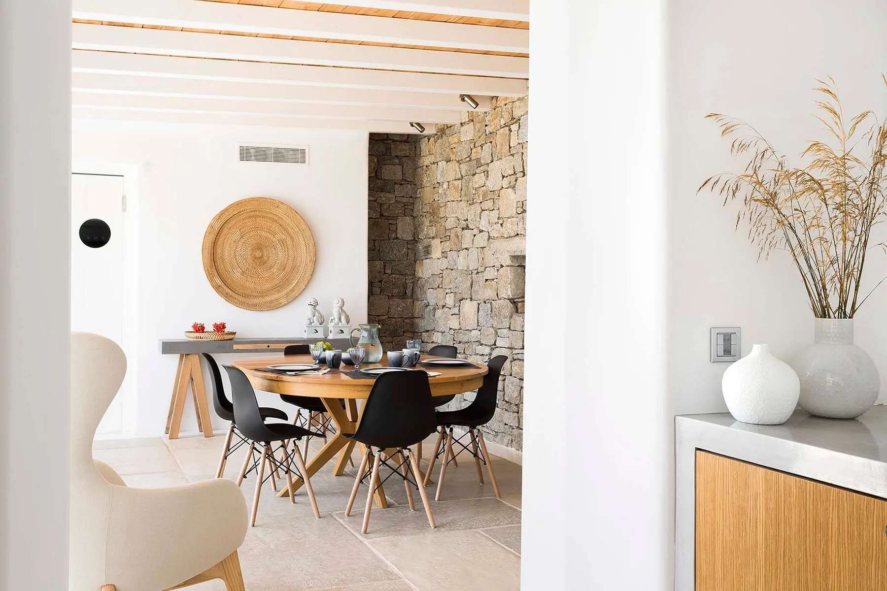 A dining area with a wooden table and dark chairs beside a stone wall.