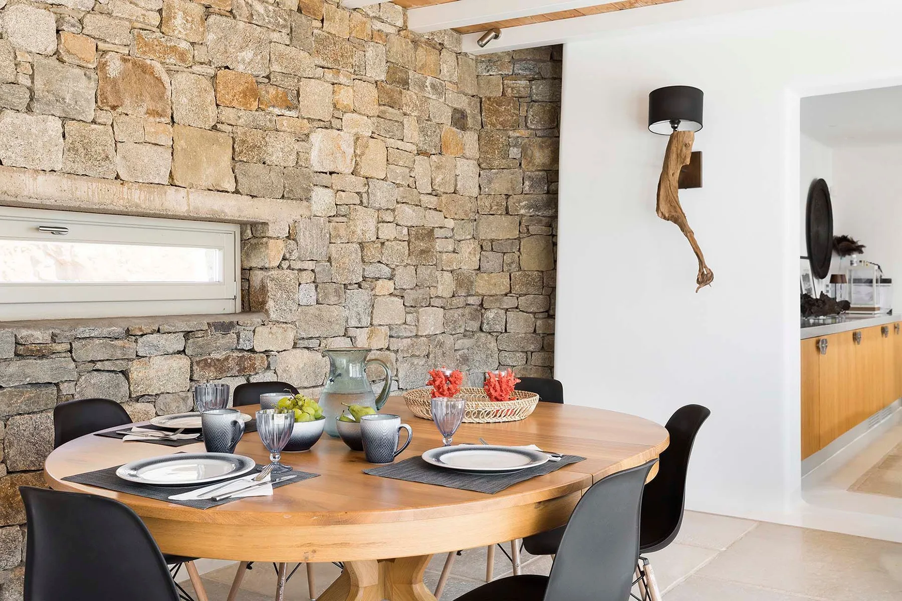 A dining area with a wooden table set with dishes beside a stone wall.