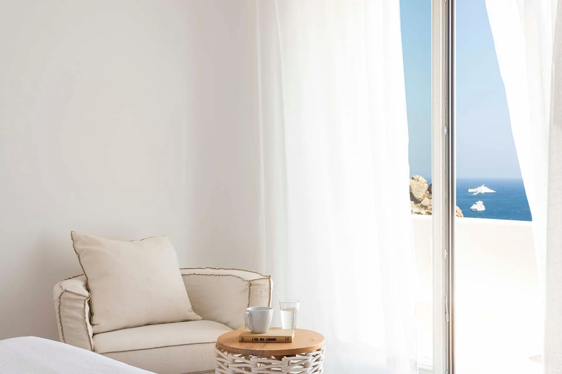 A bright living area has cushioned seating beside a window overlooking the sea.