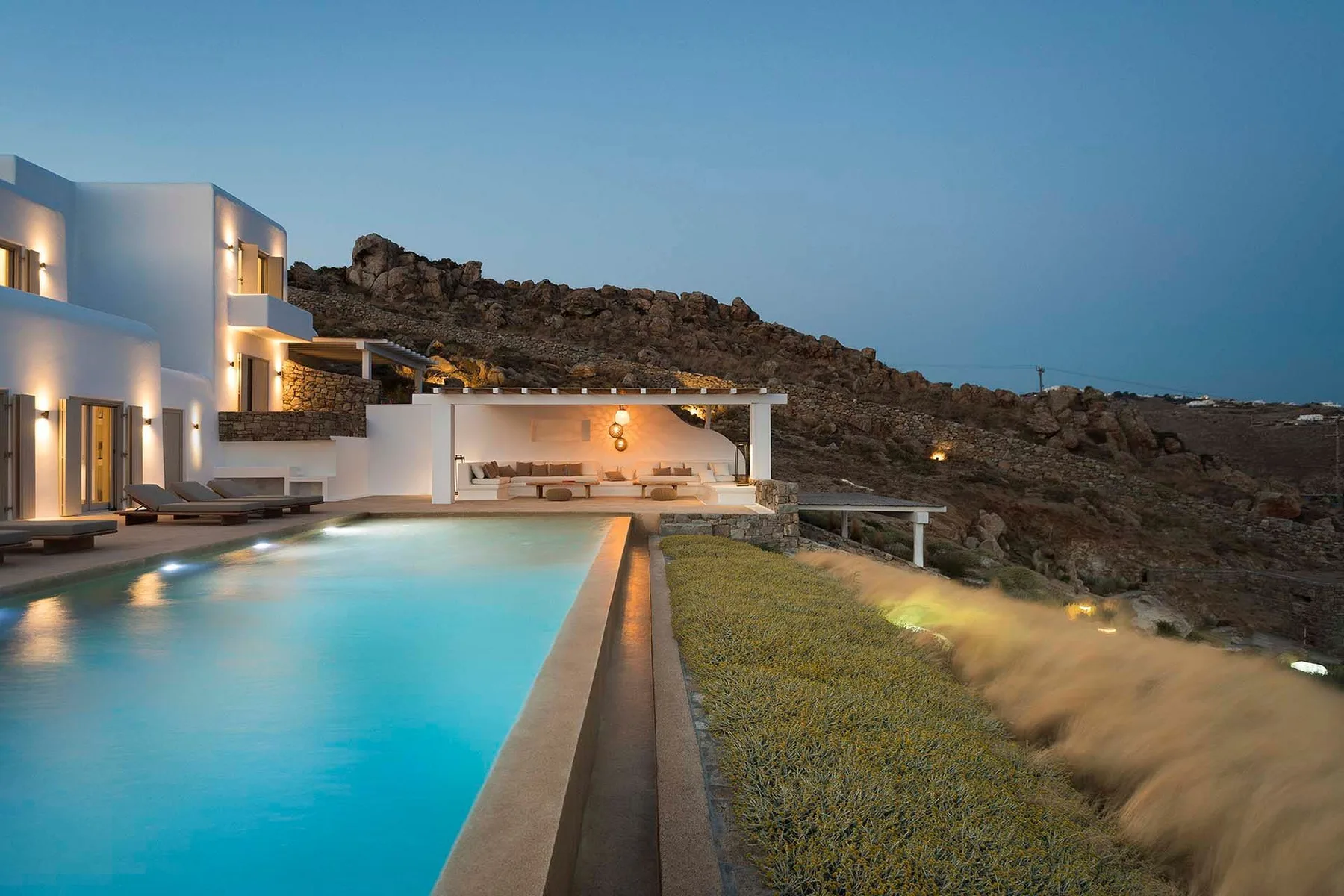 An outdoor pool beside a modern white building, with rocky hills in the background.