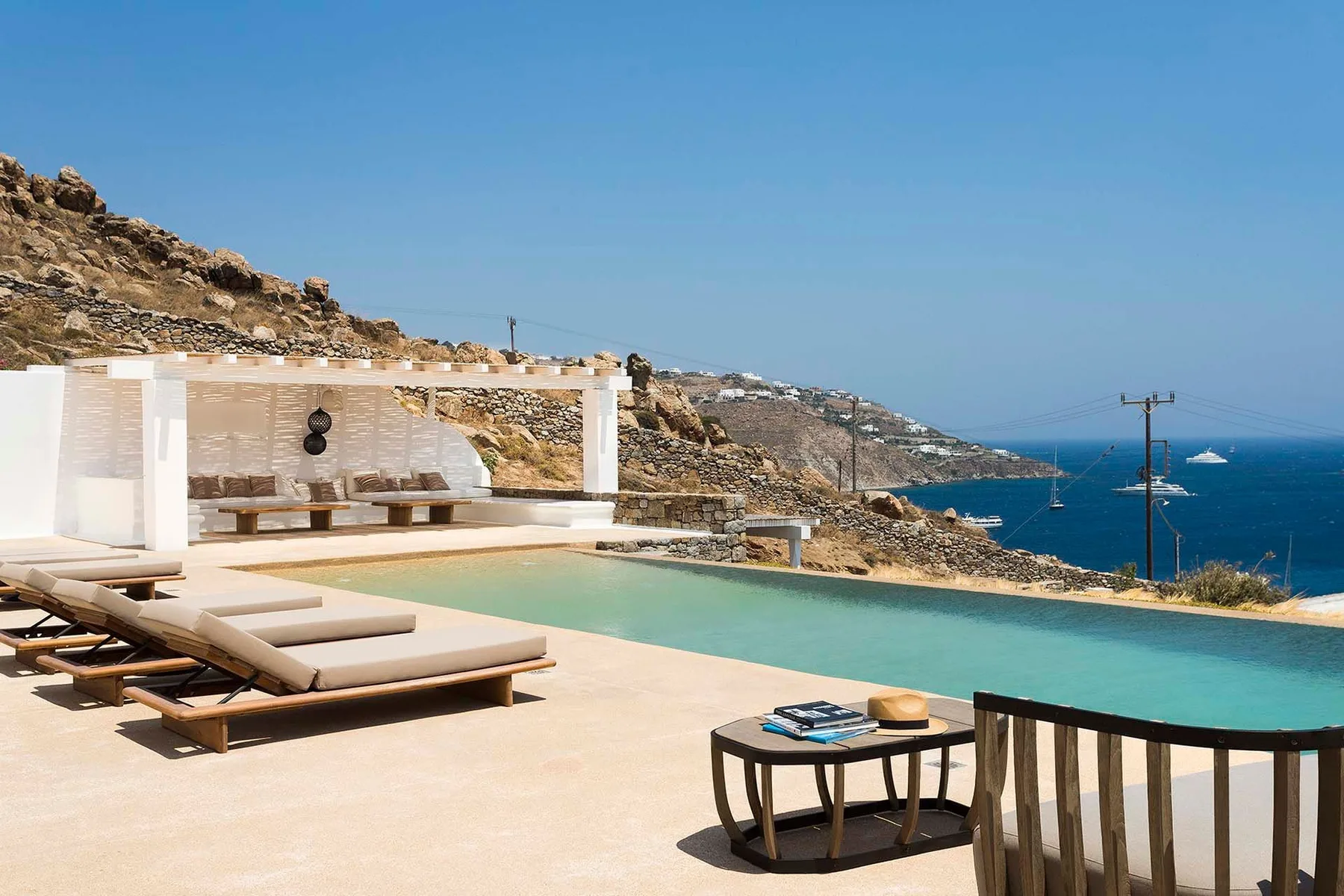 A sunlit pool terrace overlooks the sea, with loungers beside the water.