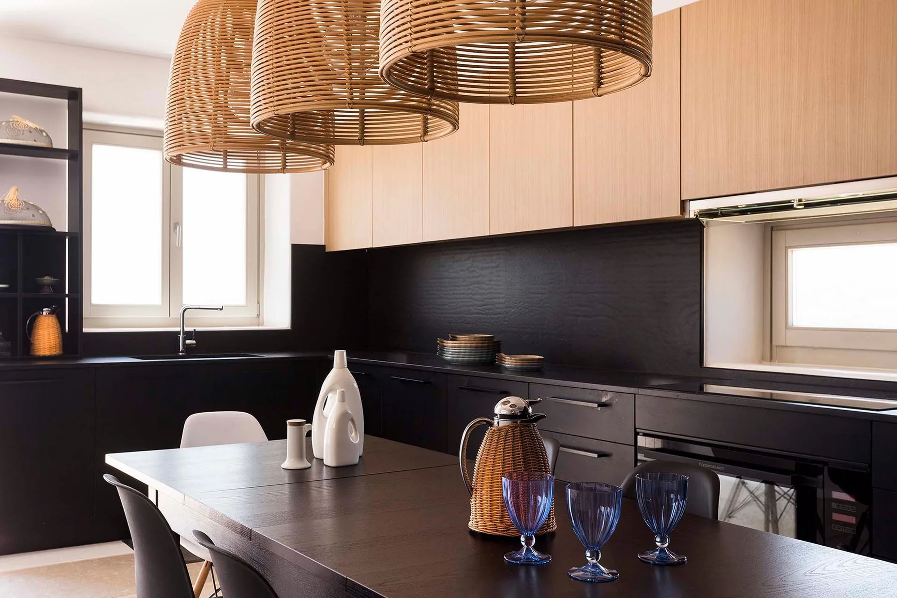 A modern kitchen with a dark island and woven pendant lights.
