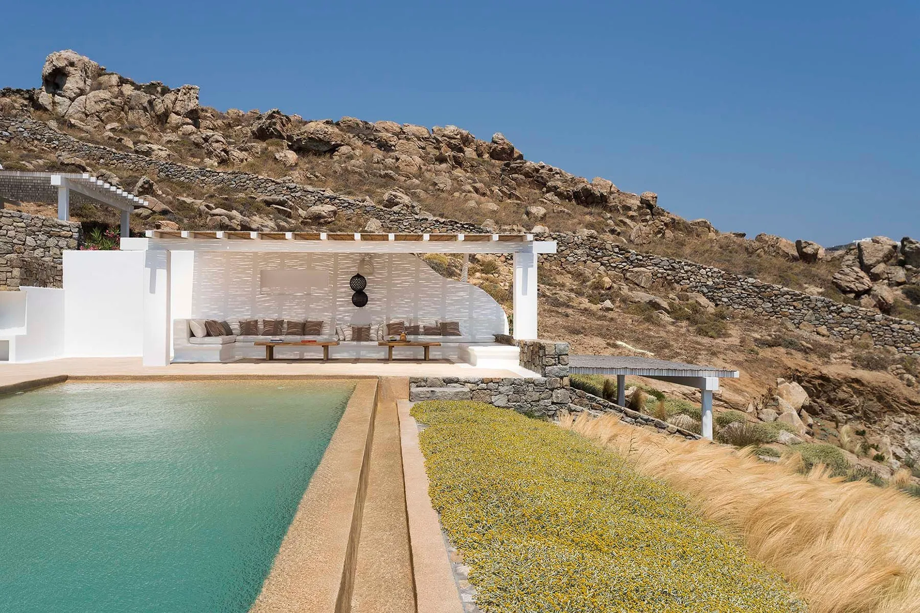 An outdoor pool beside a white shaded seating area and rocky hillside.