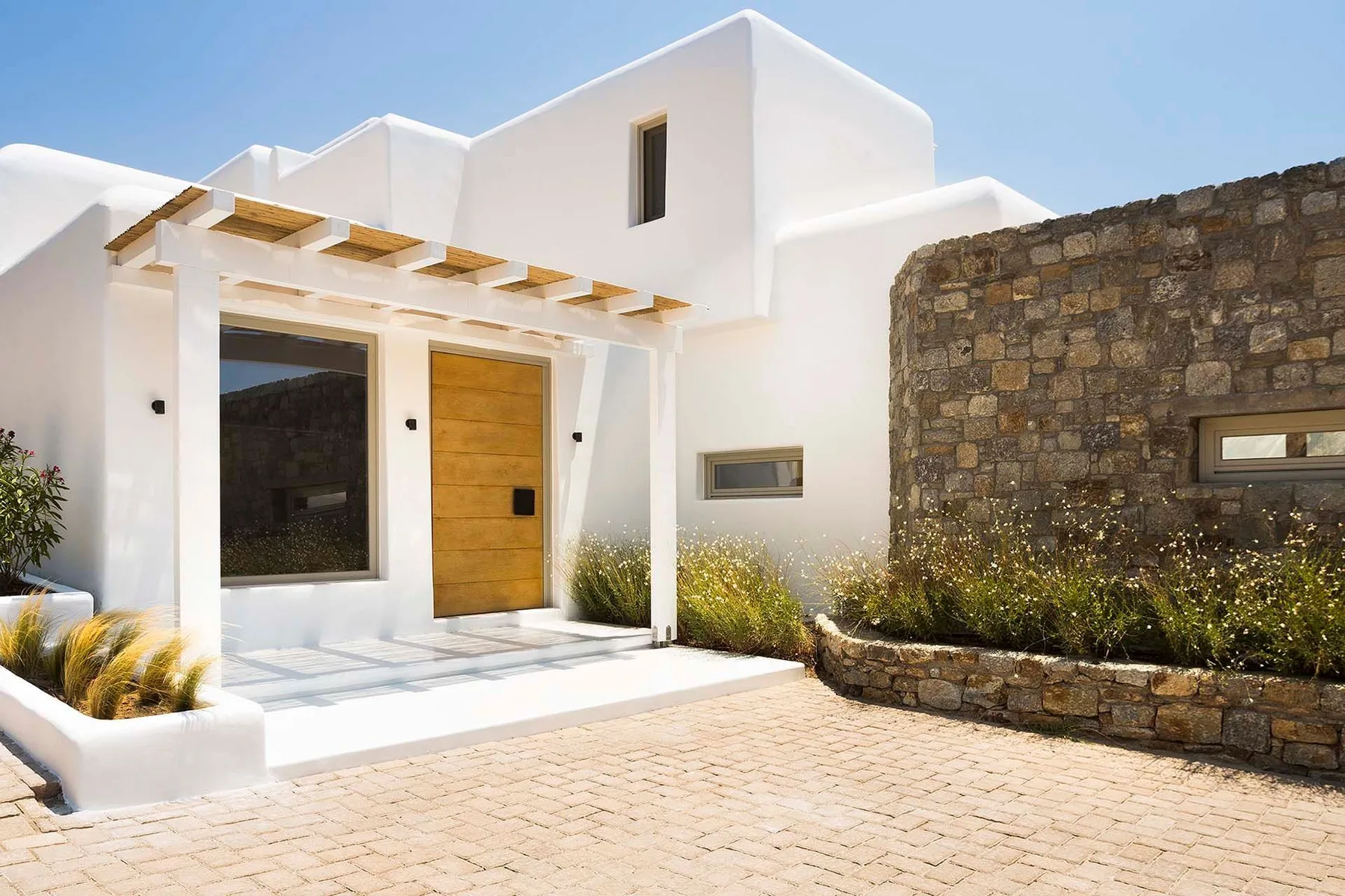 A modern white house entrance with a wooden door and stone wall.
